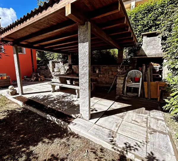 Pergola in legno con pavimentazione in pietra, tavolo e camino esterno