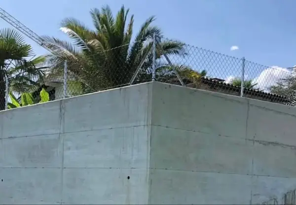 Muro perimetrale in cemento armato a faccia liscia con recinzione